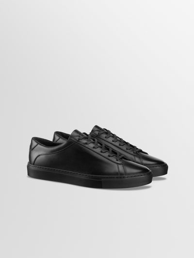 A pair of men's Italian black leather low-top sneakers with matching black laces and soles, displayed on a clean light gray background.