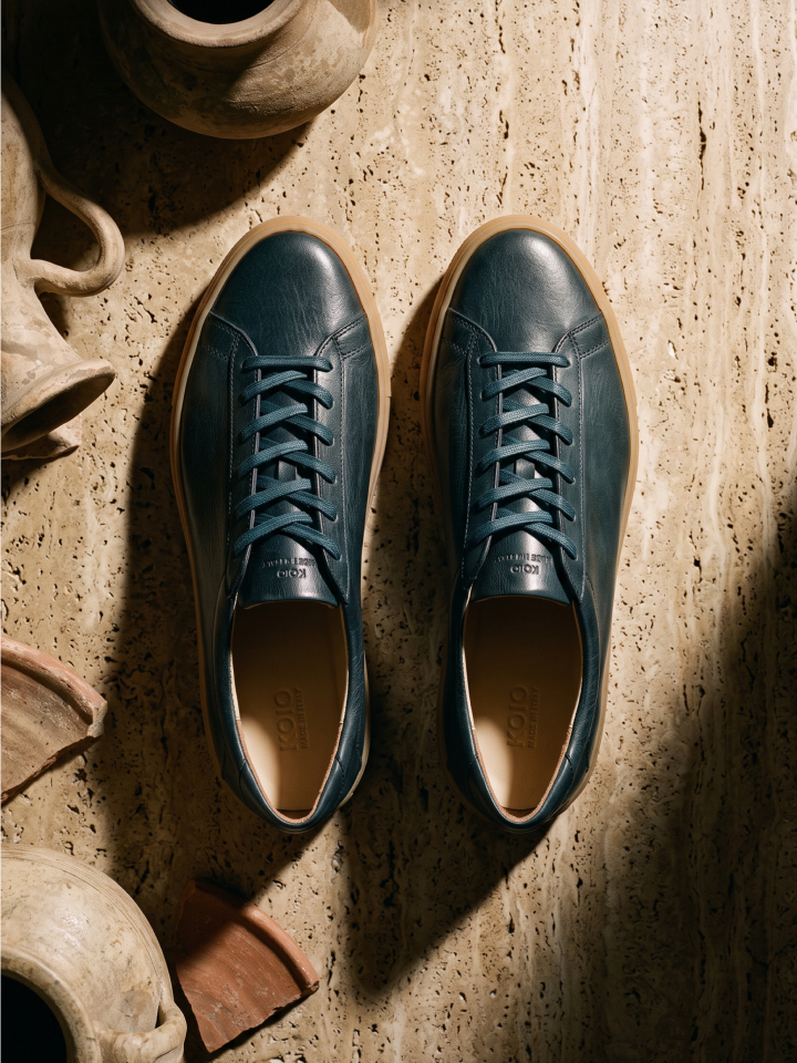 A pair of men's deep forest green Italian leather lace-up sneakers on a limestone ground with pottery around.